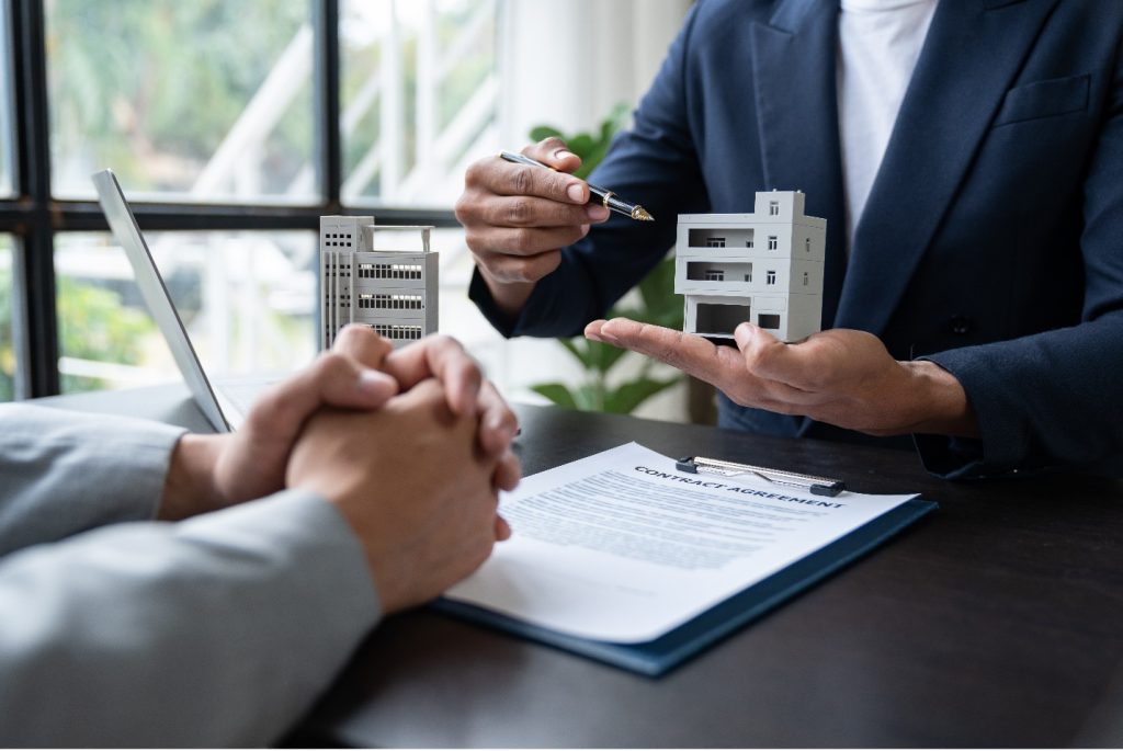 close up of two people meeting in an office next to model of a condo development. Only hands and arms visible.