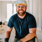 young contractor crouching on worksite and smiling with hardhat