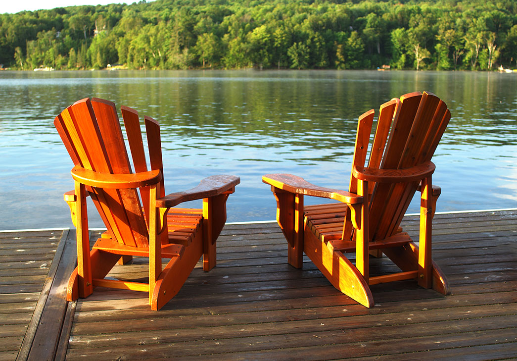 two muskoka chairs on a dock overlooking a lake