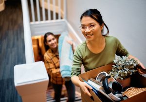 Happy Asian woman and her friend walking upstairs through hallway while moving in new apartment.